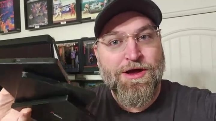 The presenter holds a stack of game cases including Xbox One, Wii, and Xbox 360 titles.