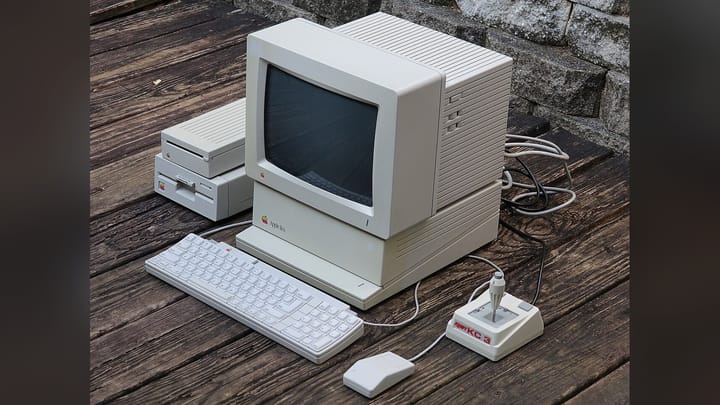 An Apple IIGS computer setup with monitor, keyboard, mouse, and disk drives